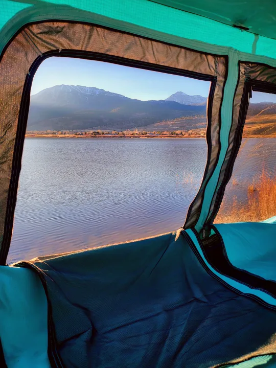 RV rental view: serene lake, snow-capped mountains, and a clear sky from a cozy tent window. Perfect escape.. Subaru Subaru Forester/Roof Top Tent 2015