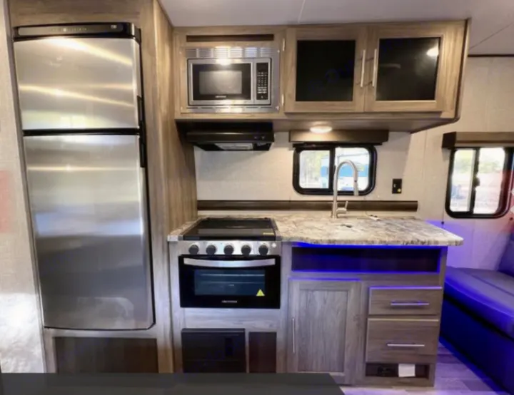 This RV rental features a compact, modern kitchen: stainless fridge, microwave, oven, sink, and ample storage.. Crossroads RV Zinger Lite 2022