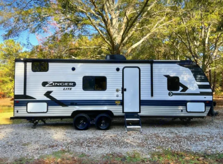 White and blue Zinger Lite travel trailer rv rental, parked on gravel outdoors, ready for your next adventure.. Crossroads RV Zinger Lite 2022