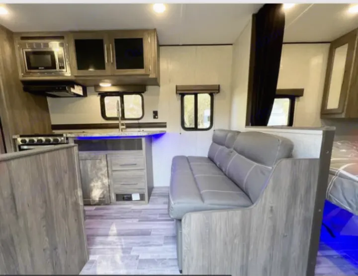 Inside a modern **rv rental**: well-equipped kitchen with a stove, microwave, sink, plus a comfy gray sofa and wood-look decor.. Crossroads RV Zinger Lite 2022