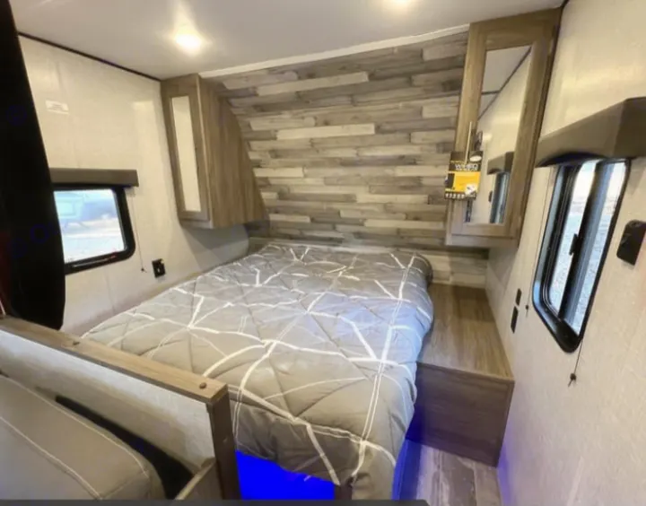 RV rental's cozy bedroom features a bed with modern wood accents, smart storage, and blue under-bed lighting.. Crossroads RV Zinger Lite 2022