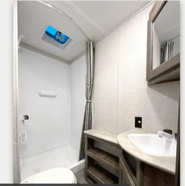 Modern RV rental bathroom featuring a shower, toilet, sink, vanity, and storage. Bright and compact for comfortable travel.. Crossroads RV Zinger Lite 2022