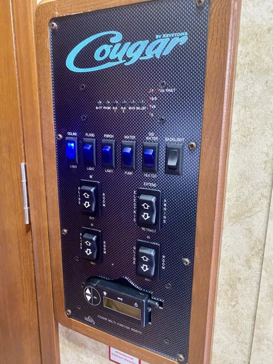 Detailed RV rental control panel shows switches for lights, water, slide-outs, and awning for easy operation.. Keystone Cougar 2012