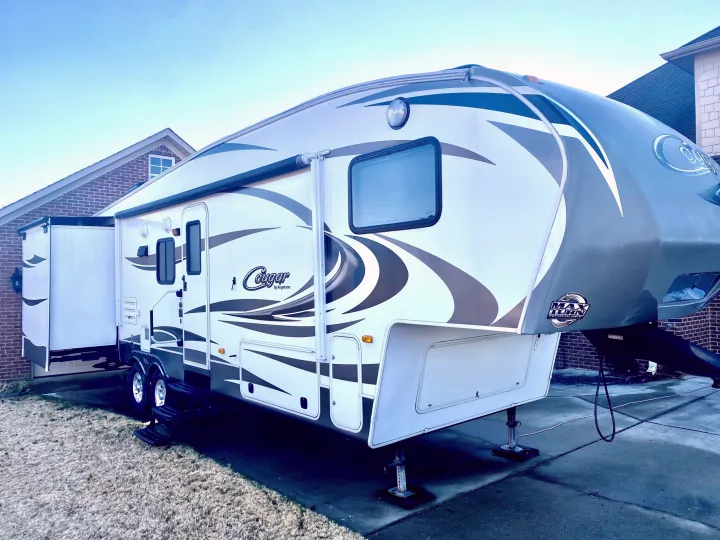White & gray Cougar fifth-wheel RV rental with slide-out extended, parked on a driveway. Ready for travel adventures!. Keystone Cougar 2012