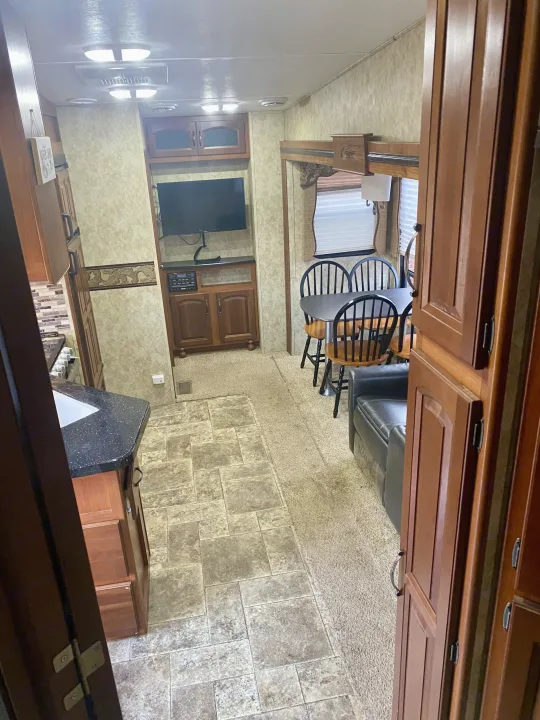 Spacious RV rental interior featuring a modern kitchen, dining area, and living space with a TV, wood cabinetry, and mixed flooring.. Keystone Cougar 2012