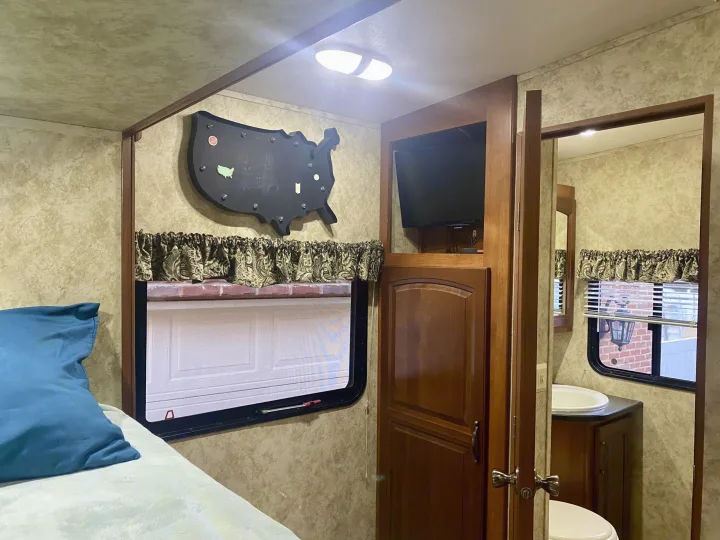 View inside an RV rental showing the bed, a US travel map, TV nook, and bathroom entrance. Ready for adventures!. Keystone Cougar 2012