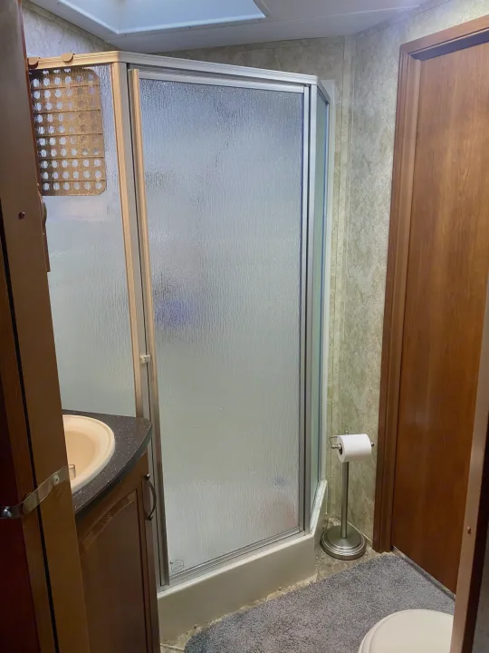 RV rental bathroom with a corner shower, sink vanity, and toilet area, featuring a freestanding toilet paper holder.. Keystone Cougar 2012