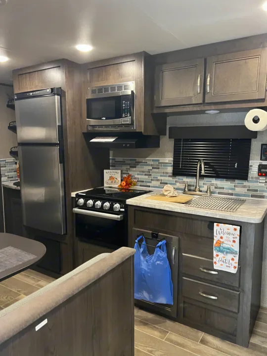 Modern RV rental kitchen with stainless steel appliances (fridge, microwave, stove, sink), mosaic backsplash, and fall decor.. Jayco Jay Flight SLX 2021