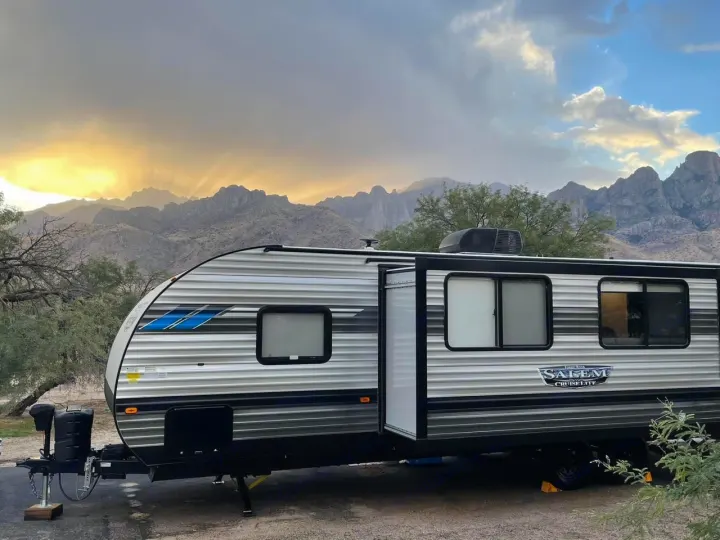 Experience nature with this RV rental! A travel trailer is parked before majestic mountains illuminated by stunning sunset rays.. Forest River Salem Cruise Lite 2022