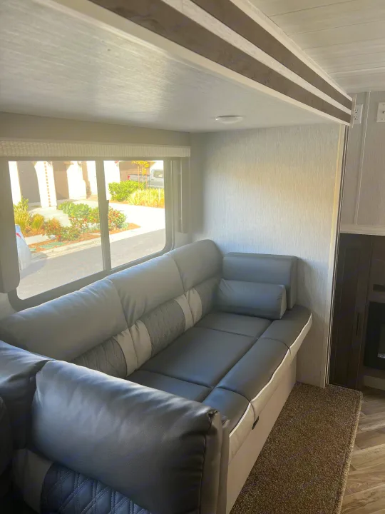 Inside an RV rental: a modern, L-shaped gray sofa by a bright window overlooking a street, offering a comfortable living space.. Forest River Salem Cruise Lite 2022