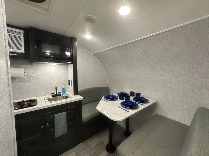 Inside an RV rental: a compact kitchen with sink, stove, microwave, and a dining booth set for four. Ideal for road trips.. Braxton Creek Bushwhacker Plus 2023