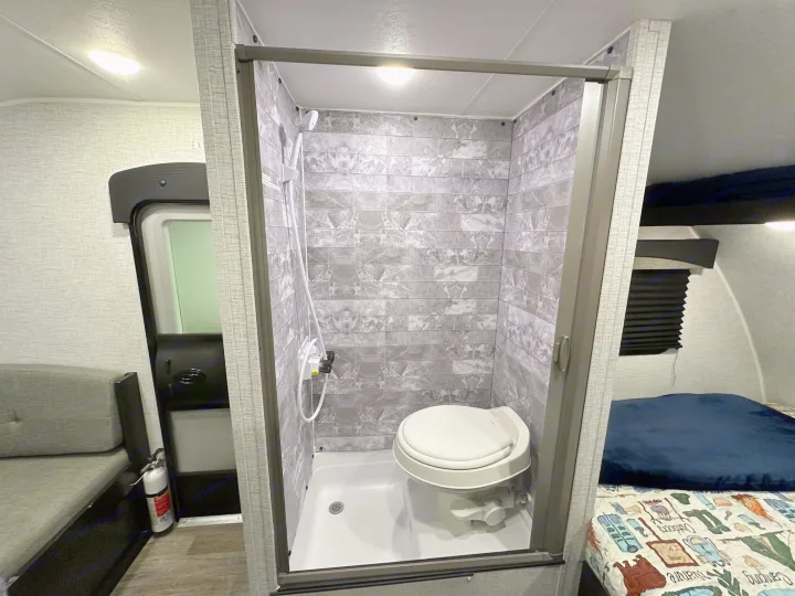 Compact RV rental bathroom with a standing shower and toilet inside. Features modern grey tiled walls for efficient space.. Braxton Creek Bushwhacker Plus 2023