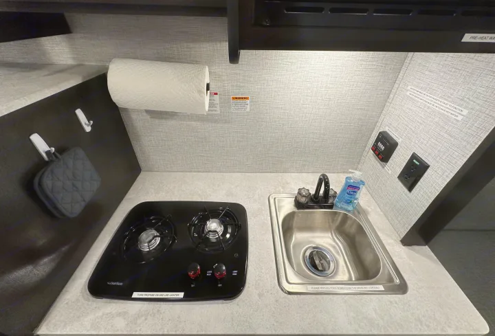 Functional RV rental kitchen setup: two-burner stove, sink, and key controls. Ready for your adventures!. Braxton Creek Bushwhacker Plus 2023