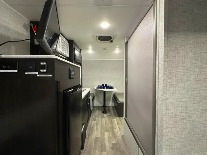 Inside a modern rv rental, featuring a compact kitchen with TV, microwave, refrigerator, controls, and a cozy dining area.. Braxton Creek Bushwhacker Plus 2023