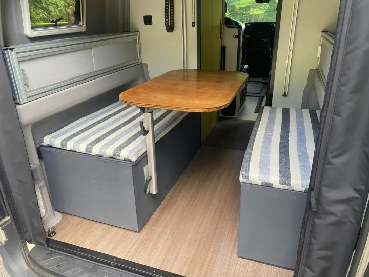 Cozy RV rental interior with striped bench seating, adjustable table, and wood-look flooring. Ready for your next adventure.. Winnebago Revel 2020