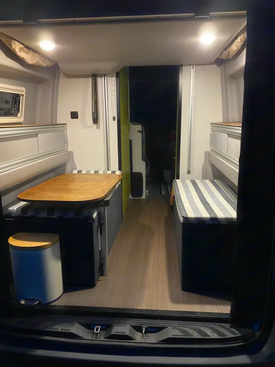 Cozy rv rental camper van interior featuring bench seating, a wooden table, overhead lights, and durable flooring.. Winnebago Revel 2020