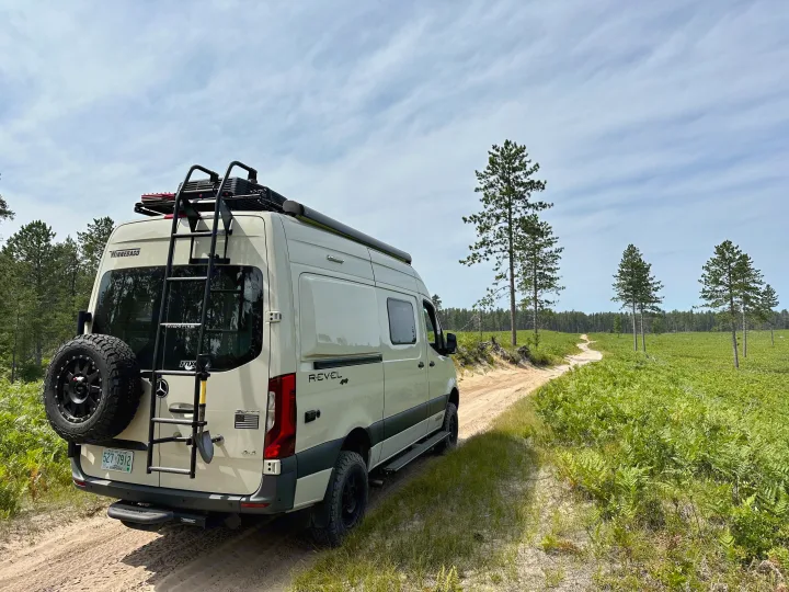 Adventure awaits! This cream Winnebago Revel **rv rental** navigates a sandy track through a vibrant green forest.. Winnebago Revel 2020