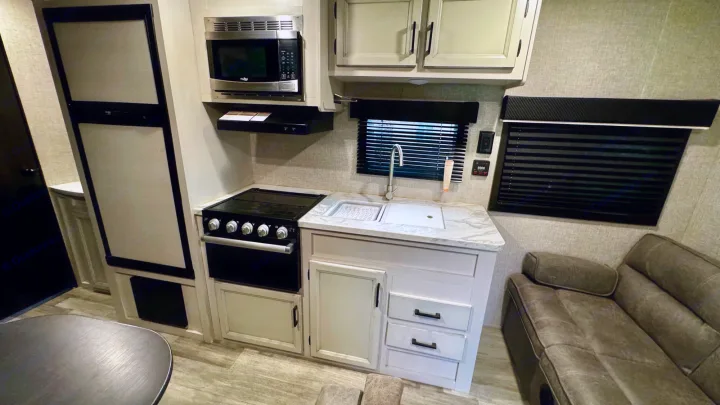 RV rental interior features a compact kitchen with microwave, stove, sink, and refrigerator, plus a comfy sofa.. Jayco Jay Flight SLX 2022