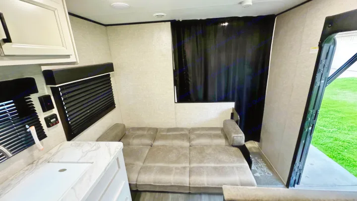 Inside this RV rental: a gray sofa bed, a white kitchenette on the left, and an open rear ramp to green grass.. Jayco Jay Flight SLX 2022