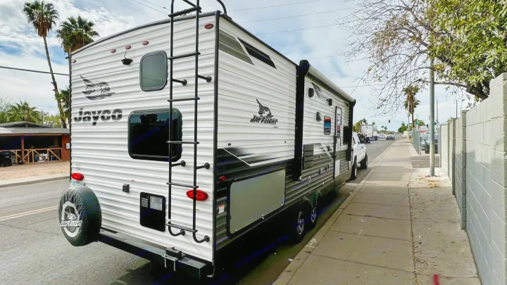 Jayco Jay Flight RV rental parked street-side. A white and gray travel trailer with rear ladder and spare tire.. Jayco Jay Flight SLX Rocky Mountain Edition 2022