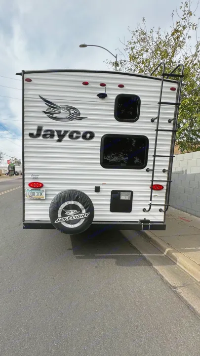 Rear view of a Jayco travel trailer, suitable for rv rental, parked on the street. Ladder and spare tire visible.. Jayco Jay Flight SLX Rocky Mountain Edition 2022
