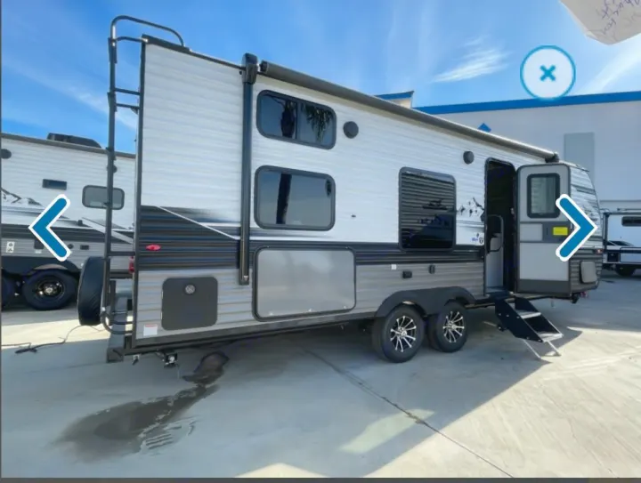 Side view of a grey RV rental travel trailer with a ladder, open door, and steps, parked on pavement. Ready for adventure!. Jayco Jay flight 2024