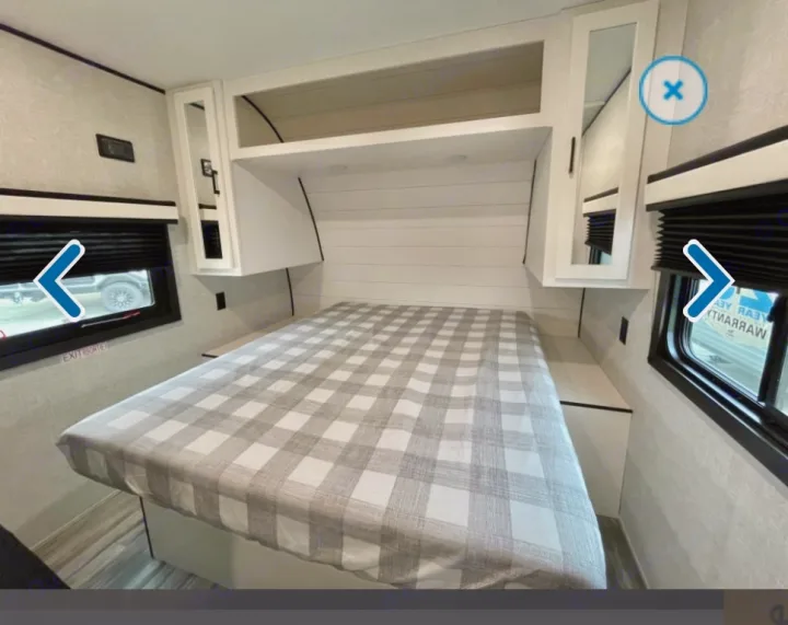 Cozy RV rental bedroom featuring a full bed with plaid cover, overhead storage, and side windows.. Jayco Jay flight 2024