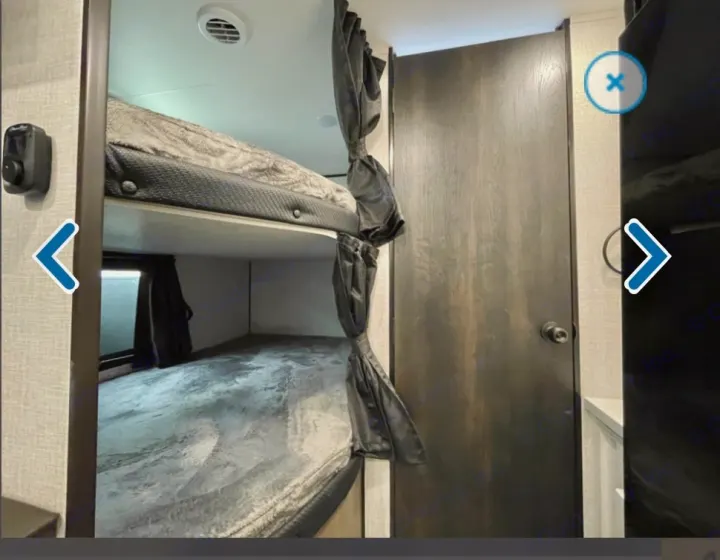 RV rental interior showing comfortable bunk beds with privacy curtains, a ceiling vent, and a closed wooden door.. Jayco Jay flight 2024
