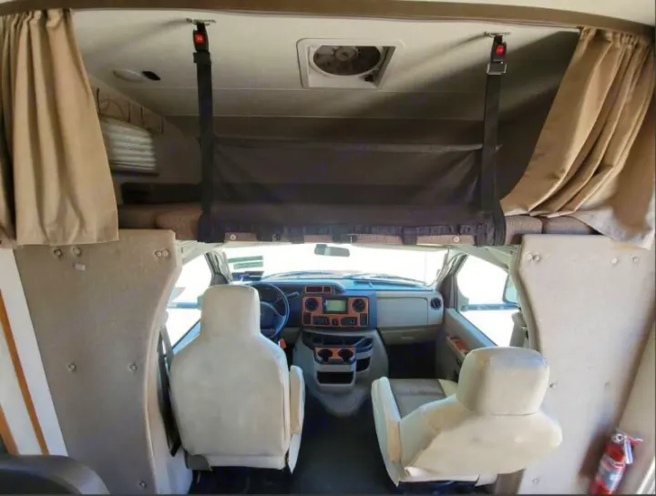 Inside an RV rental: Overhead bunk with safety net, front driver/passenger seats, and dashboard of the motorhome cockpit.. Other Other 2019