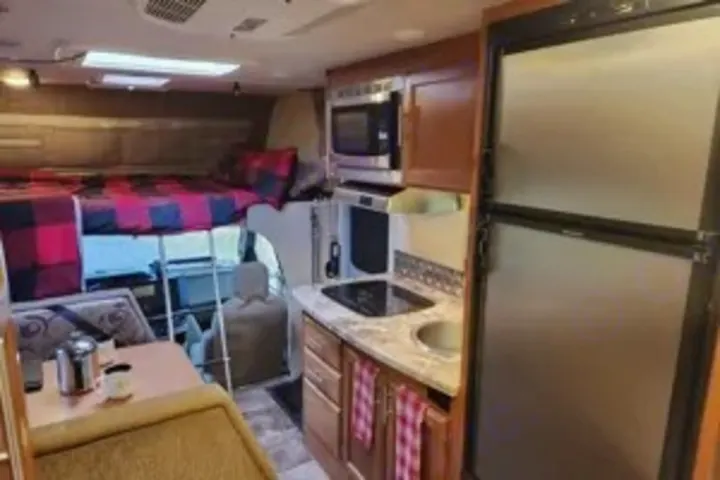 RV rental interior shows a cozy overhead bunk, kitchen with microwave & fridge, and a dining area.. Adventurer Adventurer Motorhome 2017