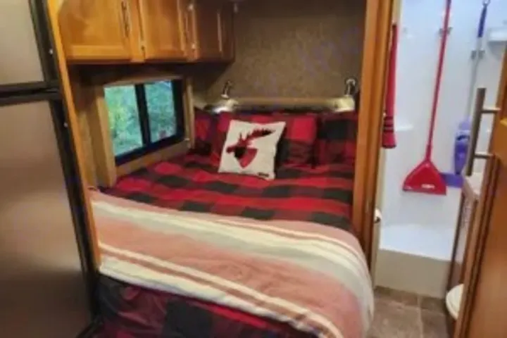 Cozy RV rental bedroom with red plaid bedding & moose pillow. Compact bath and fridge visible. Ideal for camping & travel adventures!. Adventurer Adventurer Motorhome 2017