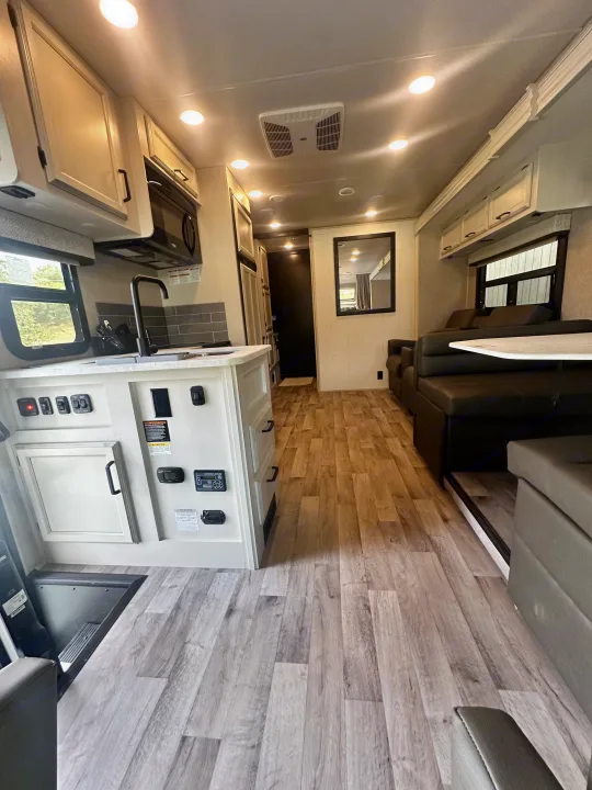 Spacious, modern RV rental interior with light wood-look flooring. Features a full kitchen, living area with comfortable seating.. Jayco Greyhawk 2023