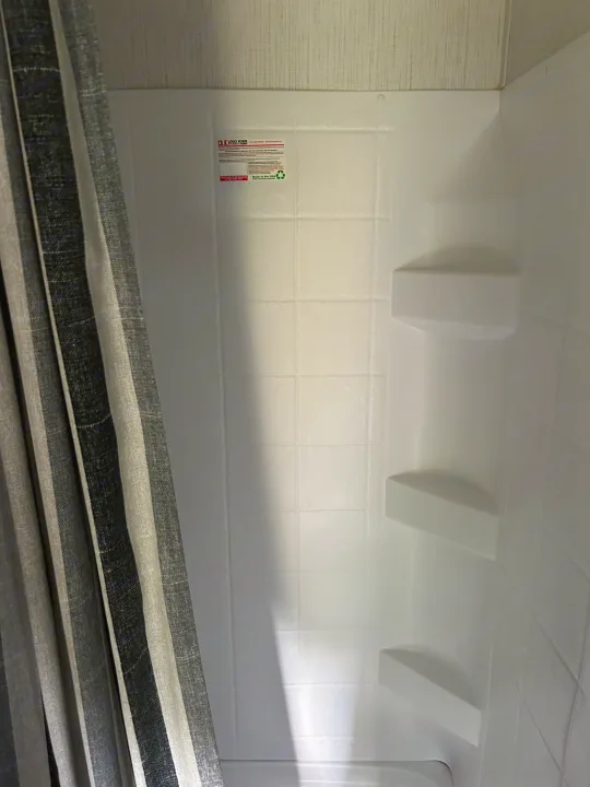 Clean white shower stall with built-in shelves and striped curtain, perfect for an rv rental.. Heartland Lithium 2021