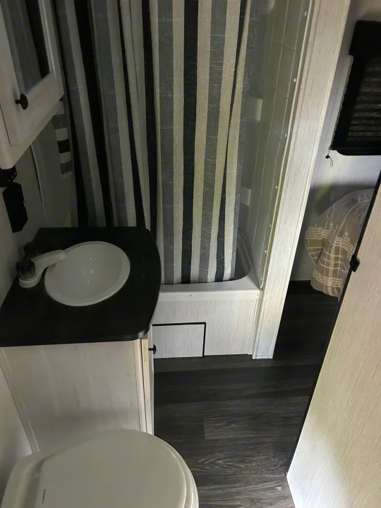 RV rental: Functional and stylish compact bathroom with sink, toilet, and modern striped shower curtain, plus glimpse of bed.. Heartland Lithium 2021
