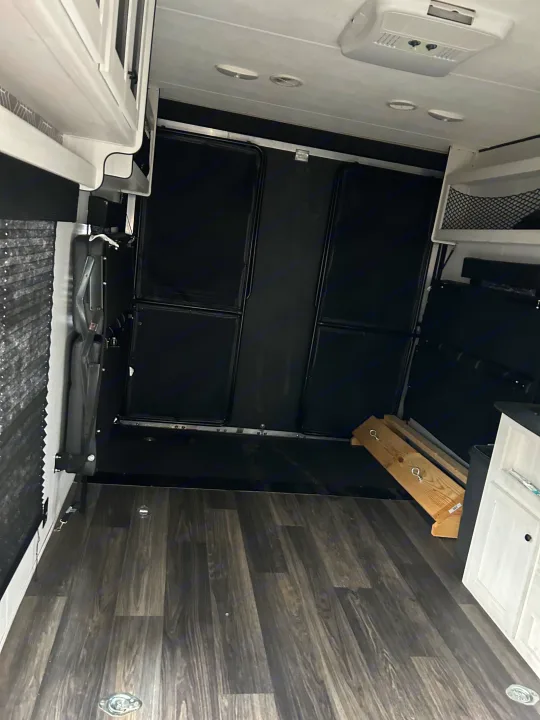 RV rental interior, showing versatile cargo space, fold-down beds, and wood-look flooring.. Heartland Lithium 2021