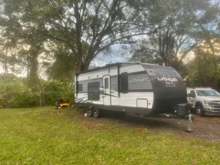 This LITHIUM travel trailer, an RV rental, is parked in a lush, treed area, ready for an outdoor adventure.. Heartland Lithium 2021
