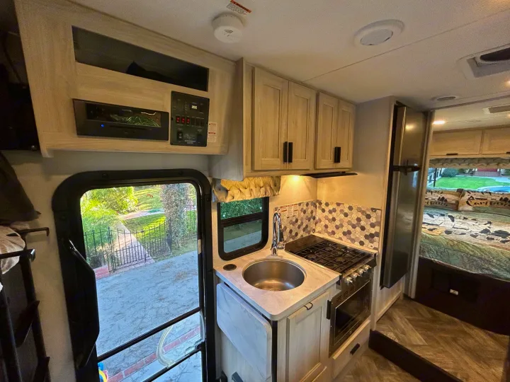 Explore this modern rv rental's compact kitchen with sink, stove, fridge, and cozy bedroom space.. Forest River Sunseeker LE 2022