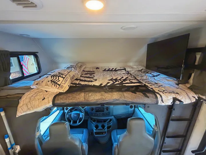 Cozy RV rental interior with an over-cab bunk bed, front cockpit, and TV. Perfect for travel adventures!. Forest River Sunseeker LE 2022