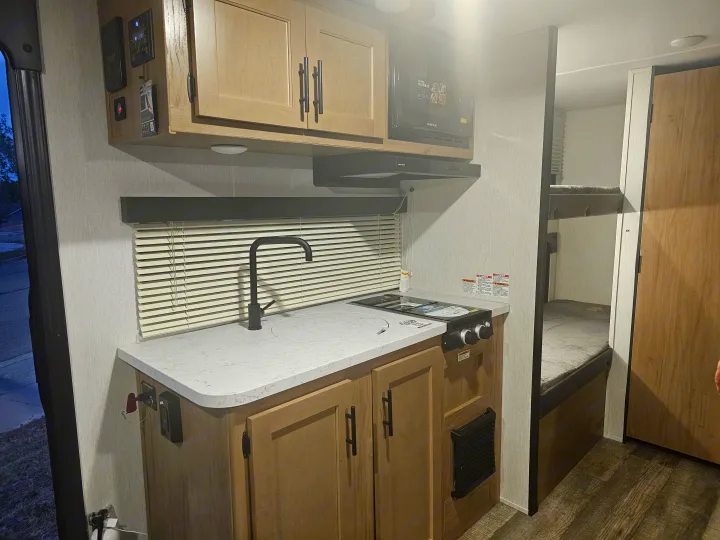Interior of a modern rv rental featuring a compact kitchen with a sink, stove, microwave, and visible bunk beds.. Forest River Cherokee Wolf Pup 2023