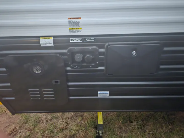 Side view of an RV rental showing fresh and city water connections, exhaust vents, and warning labels.. Forest River Cherokee Wolf Pup 2023