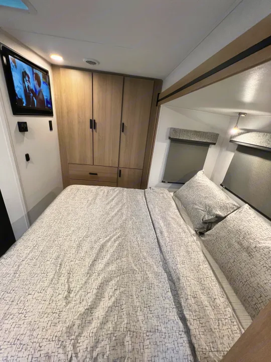 This RV rental bedroom features a comfy patterned bed, wall-mounted TV, and built-in wood cabinets.. Forest River Sunseeker 2024