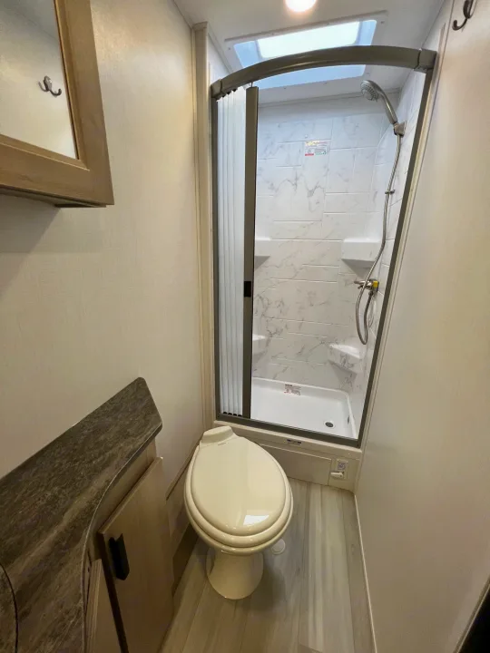 Clean, compact **rv rental** bathroom features a stand-up shower with enclosure, toilet, & vanity.. Forest River Sunseeker 2024