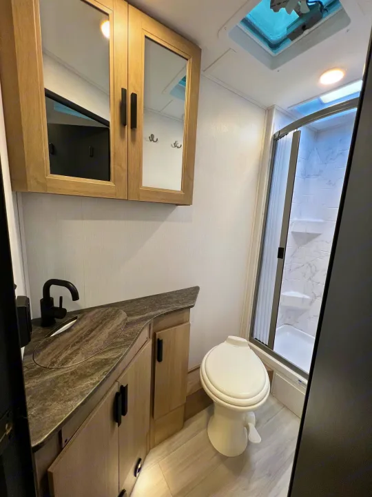 Modern RV rental bathroom: vanity, black faucet, toilet, and shower with marble-look walls. Compact and functional design.. Forest River Sunseeker 2024