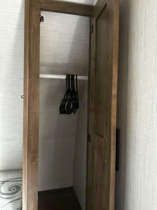 RV rental interior: an open wooden closet with a hanging rod and black hangers, offering practical storage space.. Heartland RVs Pioneer 2024