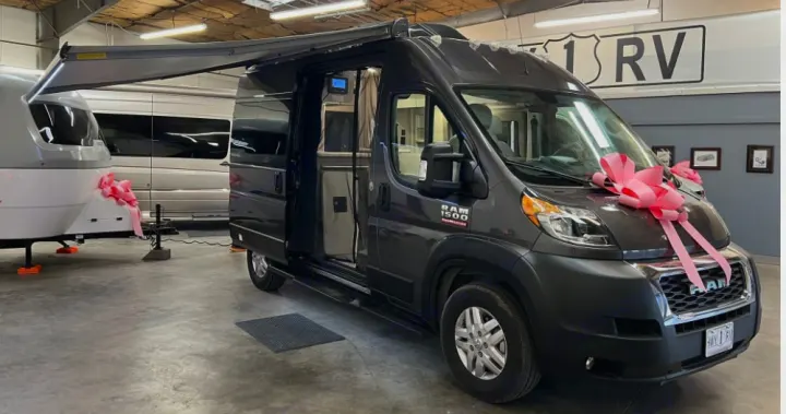 Dark gray Ram ProMaster camper van, perfect for RV rental, with an open door & extended awning next to a white trailer.. Thor Scope 2023
