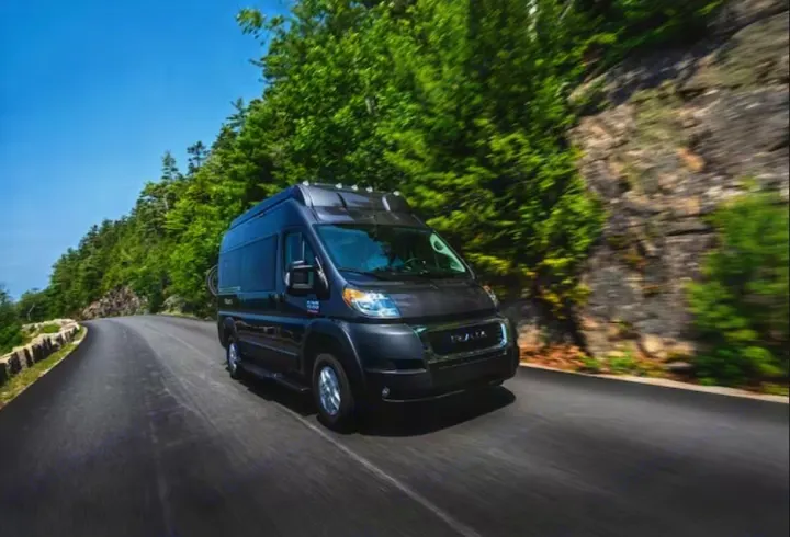 Experience nature with this black camper van RV rental, driving on a winding road through green forests. Your road trip awaits!. Thor Scope 2023