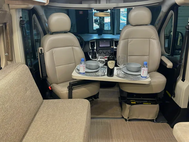 Cozy rv rental interior featuring swiveled front seats, a dining table with wine & water, and a comfortable bench seat.. Thor Scope 2023