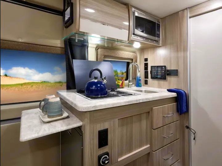 Compact, modern RV rental kitchen featuring a stove, sink, microwave, and extendable counter, ideal for travel.. Thor Scope 2023