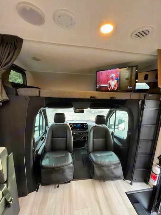 RV rental interior showing the front cab's two seats, dashboard, and the elevated bunk bed with a TV in this motorhome.. Forest River Sunseeker 2024