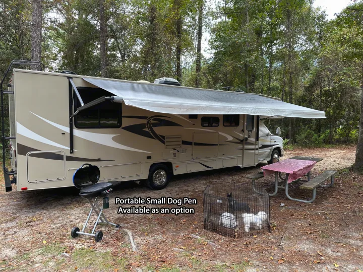 RV rental at a wooded campsite with an extended awning, grill, picnic table, and an optional dog pen with three dogs.. Forest River Coachmen Leprechaun 2015